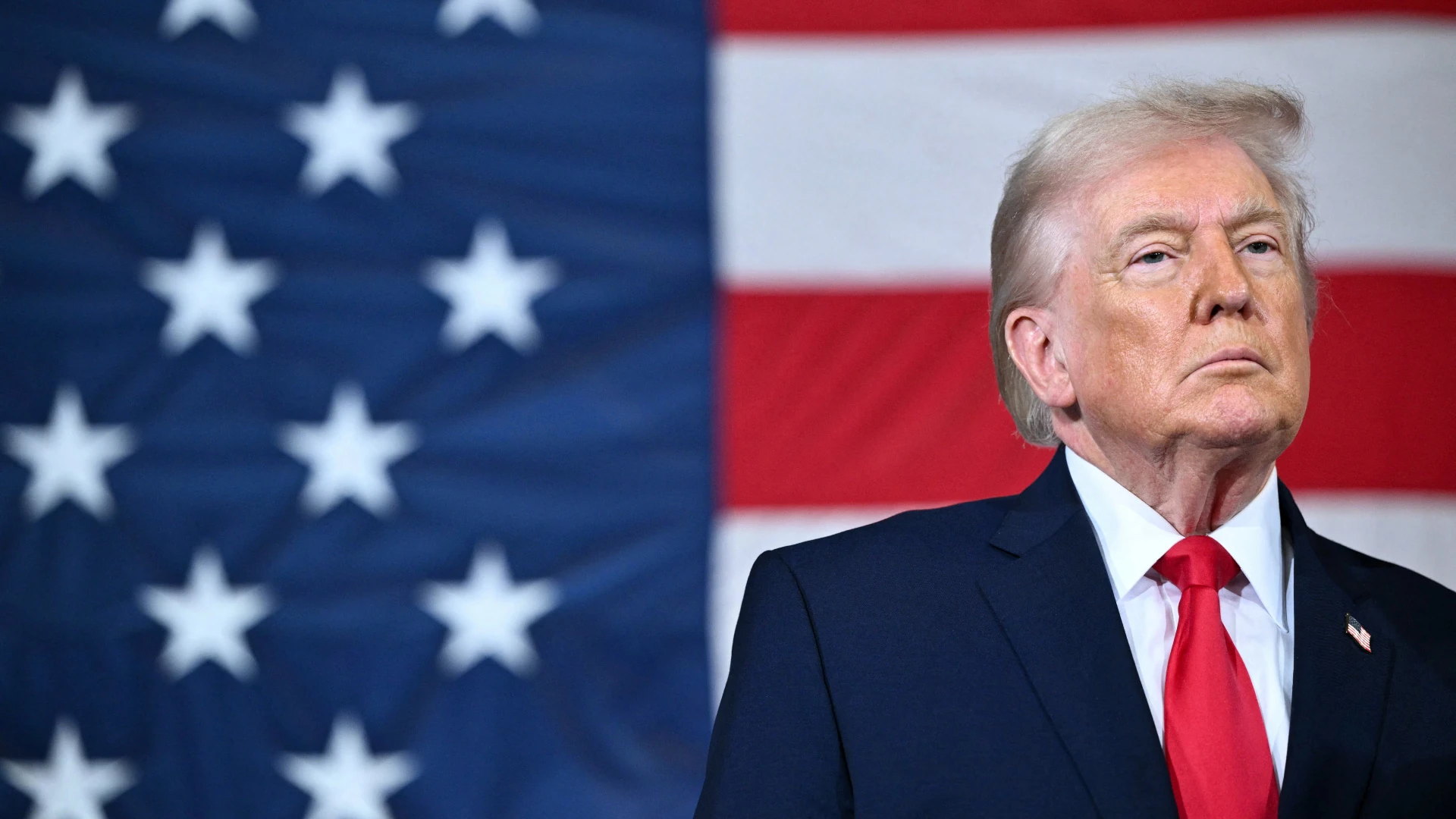 Дональд Трамп на тлі державного прапора США та телевізійного екрана з рекламним роликом
